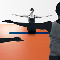 Yoga teacher kneeling at front of class, arms outstretched, eyes closed